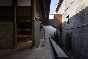 A rendered image of a modern building with a stone wall, wooden bench, and potted plants, conveying a calm and organized atmosphere