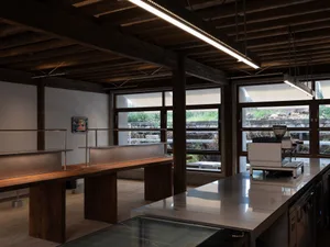Industrial kitchen with wooden floors and walls, featuring a large window, two sinks, and a refrigerator, with a clean and organized atmosphere