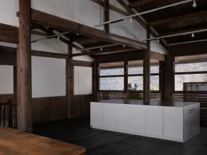 Open kitchen with wooden floors, white cabinets, and natural light from large windows, featuring a sink and dining table