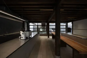 Rustic industrial kitchen with a wooden dining table, chairs, coffee makers, sink, and refrigerator