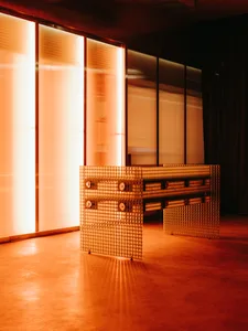 Modern living and dining space with a large metal table, orange lighting, and a mix of seating areas