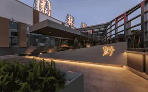 A modern Asian restaurant with a glass building, exterior signs, and potted plants, featuring a contemporary interior with gray and white tones