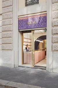 A bakery shop with a pink door, cakes on display in the window, and two women standing near the counter