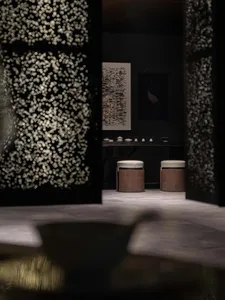 Modern showroom with a black doorway featuring a white flower pattern, a dining table, and three stools creating a cozy seating area