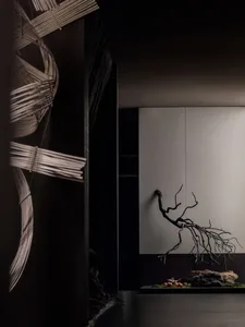 A black and white photo of a metal tree branch against a wall, creating a striking contrast between the organic form and the solid surface