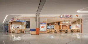 A modern restaurant with a large dining area featuring multiple tables and chairs, wood elements, and a clean appearance, with people seated and standing around