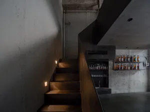 A modern staircase with metal rails and concrete walls, surrounded by bottles on different levels, conveying a contemporary and functional atmosphere