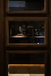 A person takes a photo of an old lamp through a window, with a wooden cabinet in the background and a nostalgic atmosphere