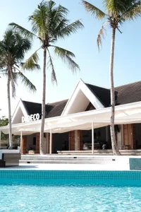 A luxurious resort scene with a swimming pool and a large open area in front of a building, featuring multiple people and two chairs for relaxation or socializing
