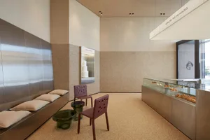 一間溫馨的烘焙店或咖啡廳，配有木質餐桌、兩把椅子，以及展示各式蛋糕，大片窗戶灑入自然光線