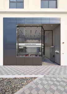 烘焙店店面外觀，玻璃窗展示蛋糕與書籍，位於溫馨的城市環境中