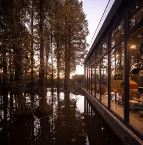 A modern building with a large glass wall and a serene surrounding environment, featuring a mix of landscaped garden and water feature