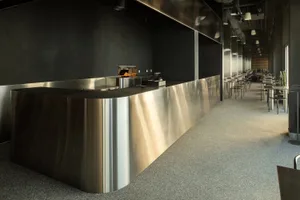 Industrial kitchen with a large stainless steel countertop, metallic finish, and several chairs for seating