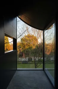 A calm office space with a black building facade, wooden benches, and a large window offering a view of trees outside