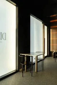 A modern showroom with a metal table surrounded by wooden chairs, natural light, and a bright atmosphere