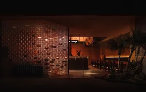 A well-lit lounge area with a bar counter and chairs, surrounded by brick walls and comfortable seating