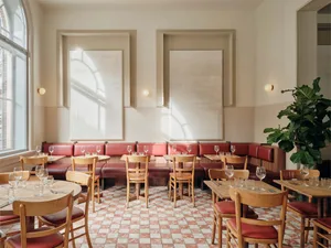 Modern restaurant interior with wooden tables, chairs, and wine glasses, featuring a mix of red and white elements