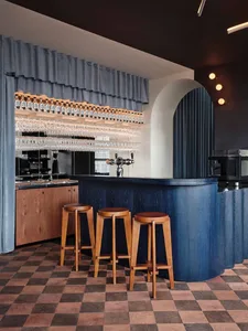 A bar area in a restaurant with a long wooden counter, stools, and wine glasses, creating a cozy atmosphere for patrons to enjoy drinks