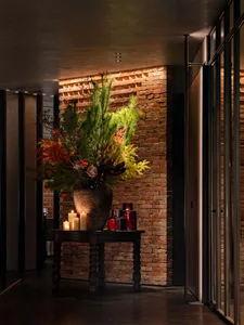 A cozy indoor space with a brick wall, wooden table, and vase with flowers, surrounded by scattered bottles