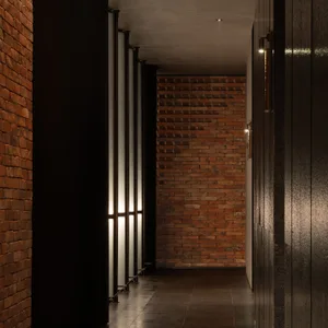 A dimly lit hallway with red brick walls, black and brown doors, and two windows providing natural light