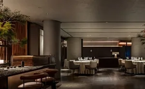 Modern restaurant dining area with multiple tables, chairs, and wine glasses, featuring clean lines and a contemporary aesthetic