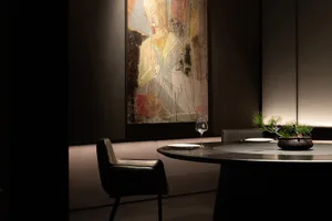 A woman's portrait in a black frame on a wall, with a dining table and chairs, wine glasses, and a potted plant in the corner