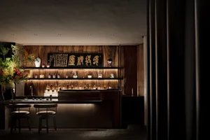 Warm and inviting Asian restaurant with wooden walls, a bar area featuring bottles of liquor, wine glasses, and decorative vases