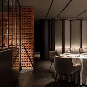 Sophisticated dining space with a large table, chairs, and wine glasses, surrounded by a brick wall and modern classic design elements