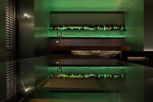 A cozy bar area with a long wooden counter, lined with bottles and wine glasses, creating an inviting atmosphere for patrons to enjoy drinks in a relaxed environment