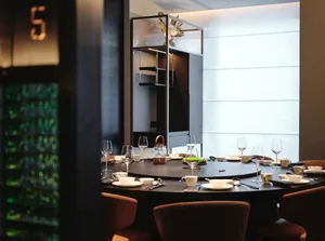 Elegant dining area with a round table, chairs, wine glasses, cups, and formal dinner settings