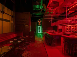 A modern bar with a red-lit atmosphere, featuring chairs and dining tables, and a stylish design
