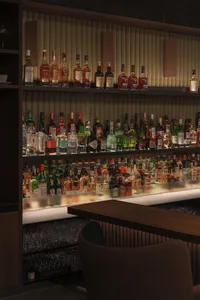 A bar scene with a wooden table and a shelf displaying a collection of liquor bottles