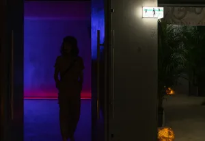 A modern living space with a woman walking through a doorway, featuring a refrigerator, potted plants, and a contemporary atmosphere