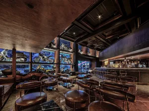 Modern restaurant interior with a black and brown color scheme, featuring a bar area with motorcycles on display, chairs, and dining tables, creating an inviting and stylish atmosphere for socializing