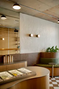 Modern restaurant interior with a counter, dining table, chairs, potted plants, and cups, featuring a welcoming atmosphere