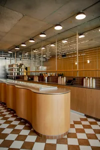 A restaurant interior with wooden floors and walls, featuring tables, chairs, and potted plants, with various items on the tables