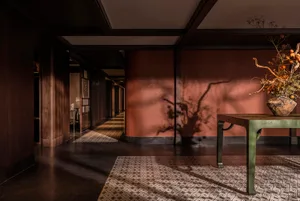 Narrow residential hallway with a green table, two chairs, and a red wall, creating a cozy atmosphere