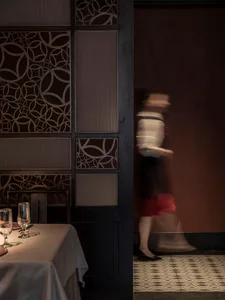 A woman in a white dress walks through a doorway into a cozy restaurant with a table and chairs, suggesting a relaxed dining atmosphere