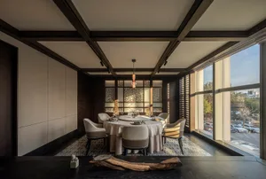Dining area with a round table set for guests, surrounded by chairs and vases, in a modern space with wooden walls and natural light