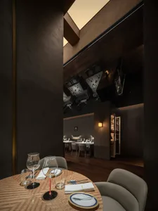 A dark and moody dining space with a wooden floor and walls, featuring a table set with chairs and wine glasses