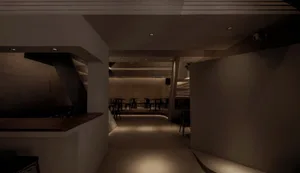Dimly lit restaurant interior with a long bar area, concrete walls, and chairs placed throughout the space