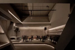 Empty modern restaurant interior with concrete walls and floors, featuring comfortable seating areas with chairs and dining tables