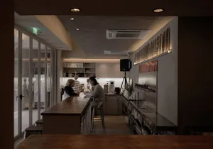 A casual restaurant bar area with patrons enjoying their time together, featuring a counter with bottles, cups, and bowls, and a refrigerator in the background