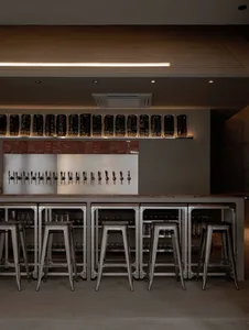 A bar area with a long wooden counter and stools, featuring beer taps and bottles, set in a social and inviting atmosphere