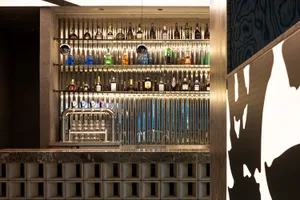 A well-stocked bar with a wooden theme, featuring a large collection of liquor bottles and wine glasses, creating a cozy atmosphere