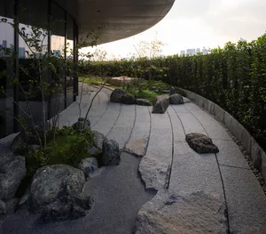 A modern building with a curved facade and a large glass wall, surrounded by potted plants and greenery