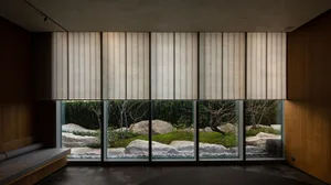 A hotel living area with large windows, vertical blinds, and potted plants, offering a calm and inviting atmosphere with a focus on the connection between interior and exterior spaces
