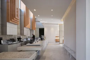 Empty restaurant kitchen with white walls and floors, featuring tables, chairs, appliances, and kitchen utensils, conveying a sense of orderliness and readiness for use