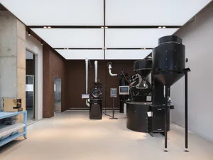 Industrial workspace with two large black silos, machinery, and a TV mounted on one of the silos