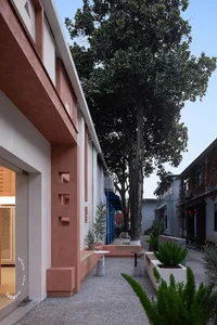 A photo of a house with a red brick exterior, a balcony, and a bench, surrounded by a tree and two potted plants